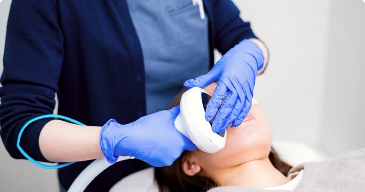 手袋を着用した施術者が患者の顔に医療機器を当て、専門的な美容施術を行っている場面